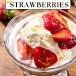 A glass dish with vanilla ice cream, strawberries in syrup, and orange zest on a wooden table.