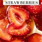 Close-up of strawberries in syrup with orange zest; a spoon rests beside the glossy, syrup-soaked fruit.