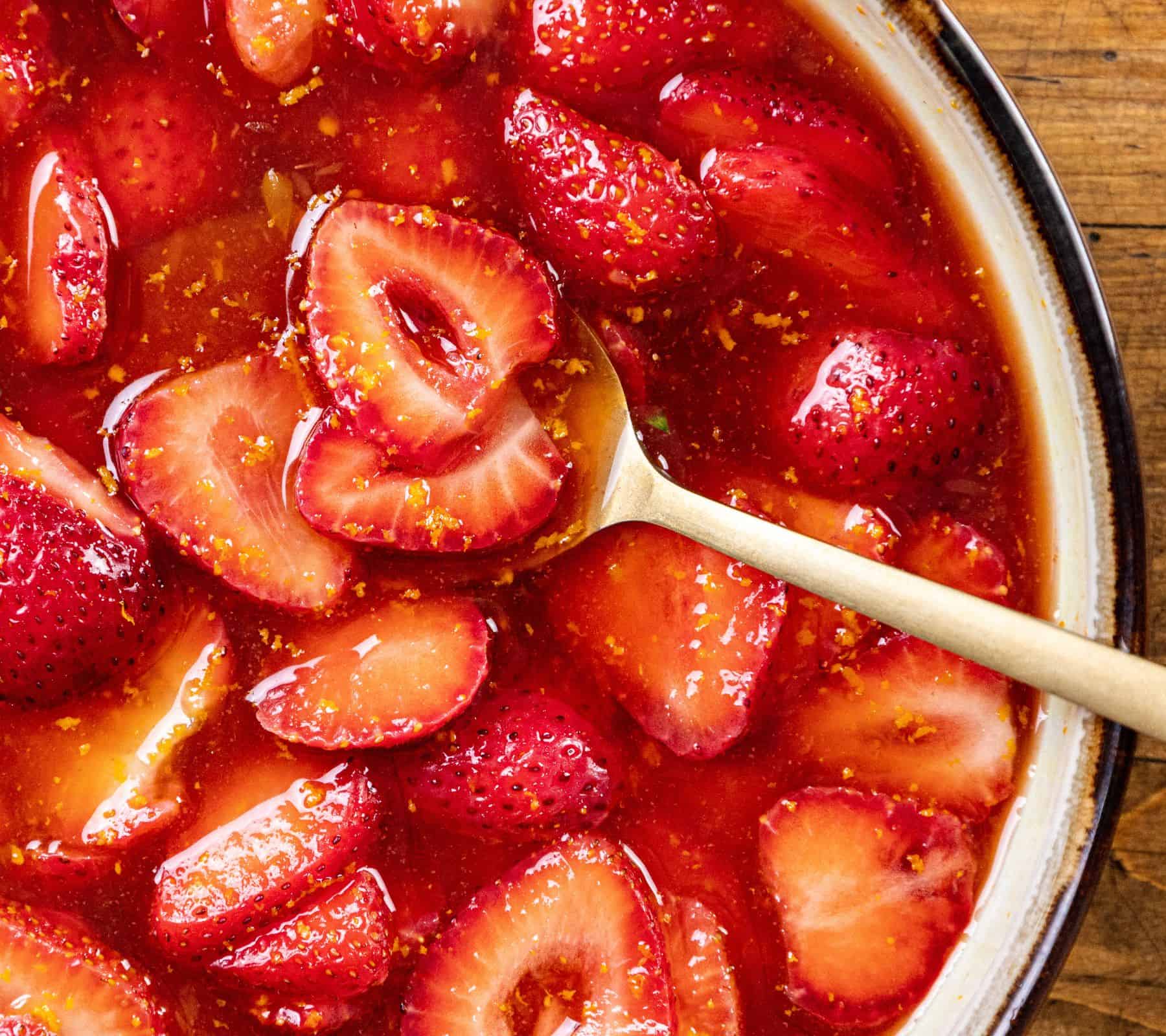 Strawberries in syrup with a spoon inside a dish, seen from above.