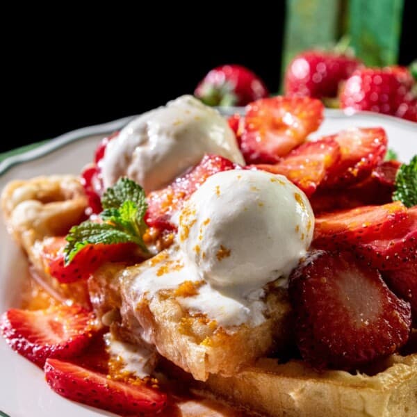 French toast on a plate with boozy strawberries, two scoops of vanilla ice cream, mint leaves, and syrup.