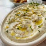A white platter loaded with whipped ricotta and garnished with olive oil and lemon zest.