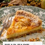 A slice of pear tart with shortbread crust on a decorative plate, topped with powdered sugar and served with a fork.