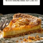 A slice of pear tart with a shortbread crust on a decorative plate, next to a fork and some scattered crumbs.