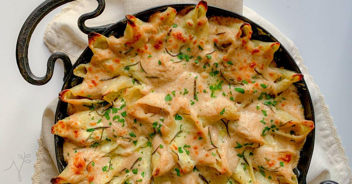 Iron roasting pan with stuffed pasta shells covered in a white sauce with herbs.