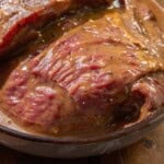 Raw beef in a bowl on a wooden surface, covered in thick brown marinade.