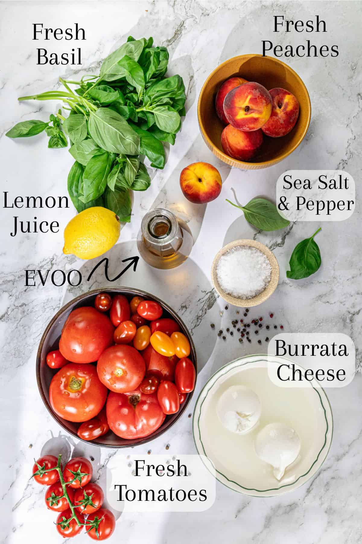 Top-down view of a salad featuring sliced tomatoes and peaches, fresh basil leaves, burrata cheese, lemon wedges, and small bowls of sea salt and pepper. The ingredients are arranged on a marble surface.