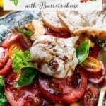 A plate with peach and tomato slices, burrata cheese, basil leaves, a drizzle of balsamic glaze, and a slice of bread.