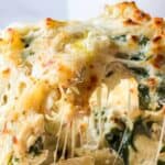A serving of cheesy chicken alfredo casserole with pieces of chicken, wilted spinach, pasta, and a layer of melted golden-brown cheese on top.