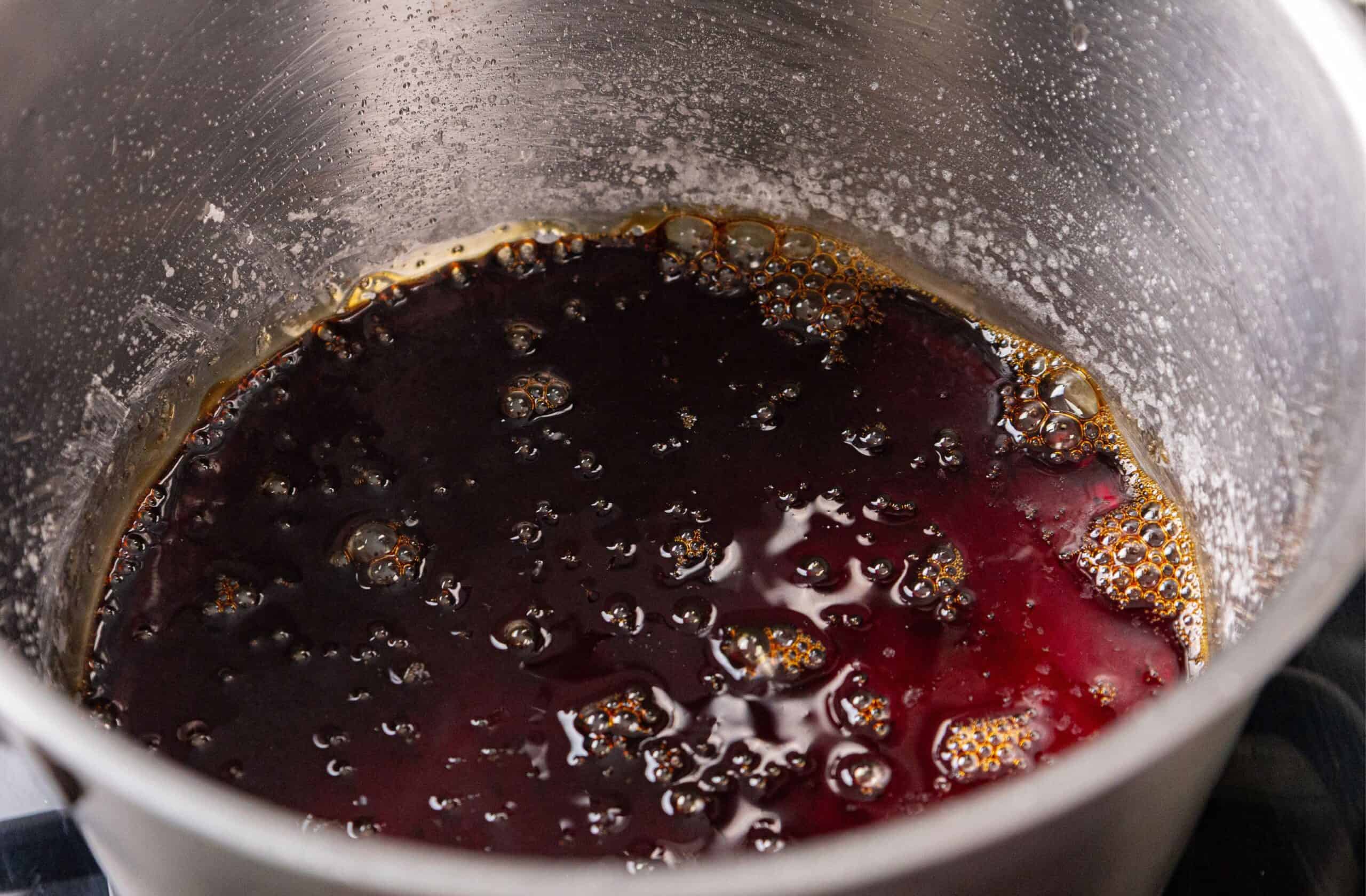 A close-up of a saucepan with dark brown custard, bubbling on the surface and residue on the pot’s sides.