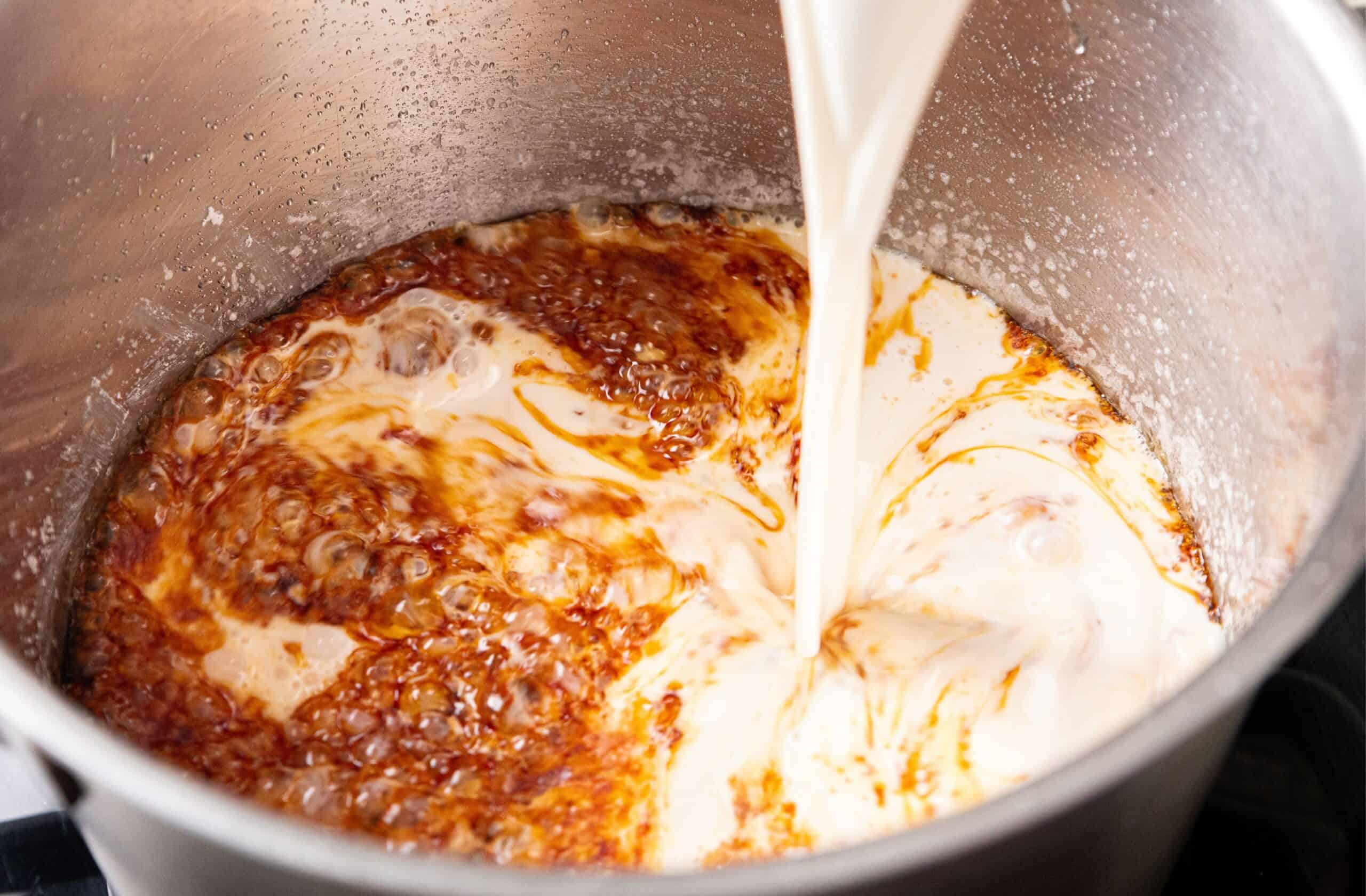 Cream pours into a pot of bubbling caramel, forming a swirling mixture.