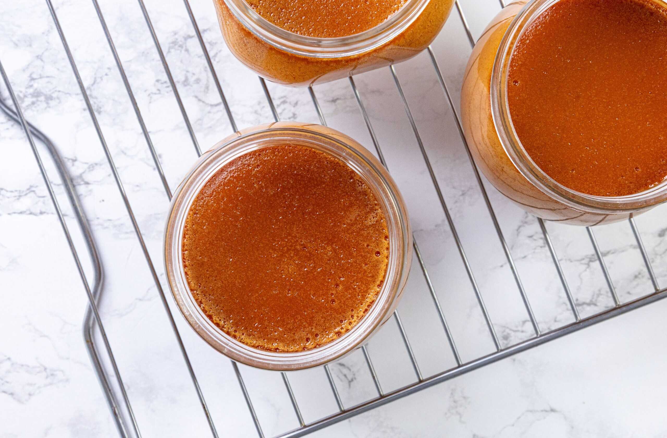 Three glass jars of caramel custard on a wire rack, sitting atop a marble surface.