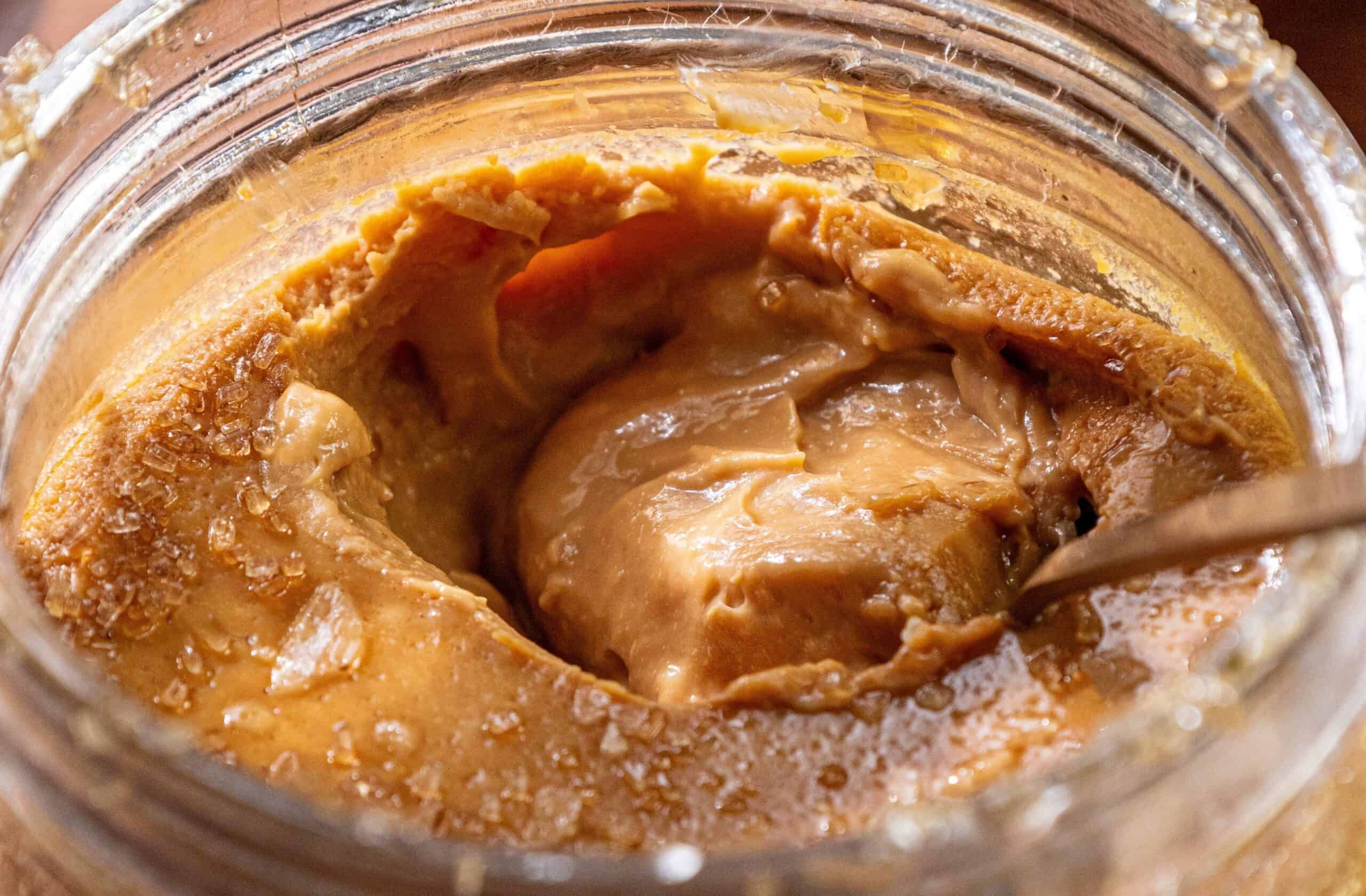 Close-up of an opened jar of peanut butter with a spoon inside and visible oil separation.