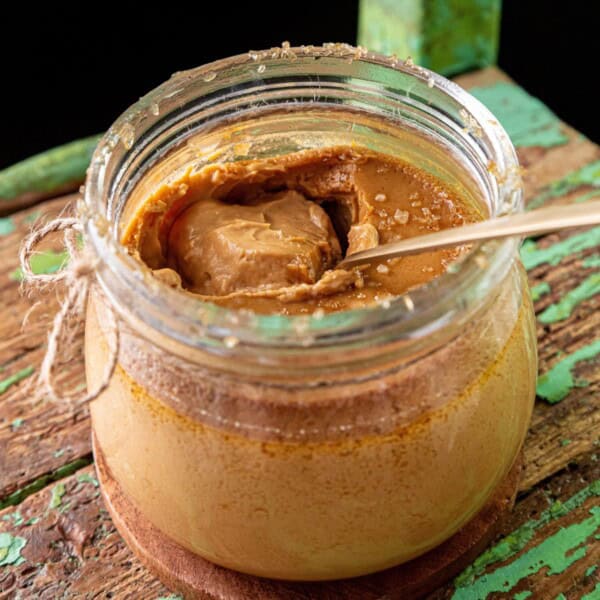 An open jar of peanut butter with a spoon inside sits on a rustic wooden surface.