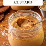 An open glass jar of custard with a spoon sits on wood, surrounded by salt crystals and a bowl of brown sugar.