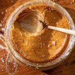 A spoon in a jar of custard topped with coarse salt and sugar, on wood with salt crystals and a piece of twine nearby.