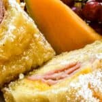 Two halves of a sandwich dusted with powdered sugar, served with cantaloupe slices and grapes.