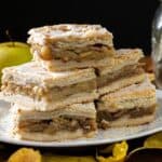 Four stacked Apple Slab Pie bars on a plate, with whole green apples and autumn leaves nearby.