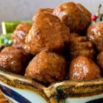 A ceramic bowl filled with round meatballs coated in a glossy, dark sauce.