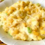 A bowl filled with a casserole containing corn kernels, diced green peppers, and a thick, creamy cheese sauce.