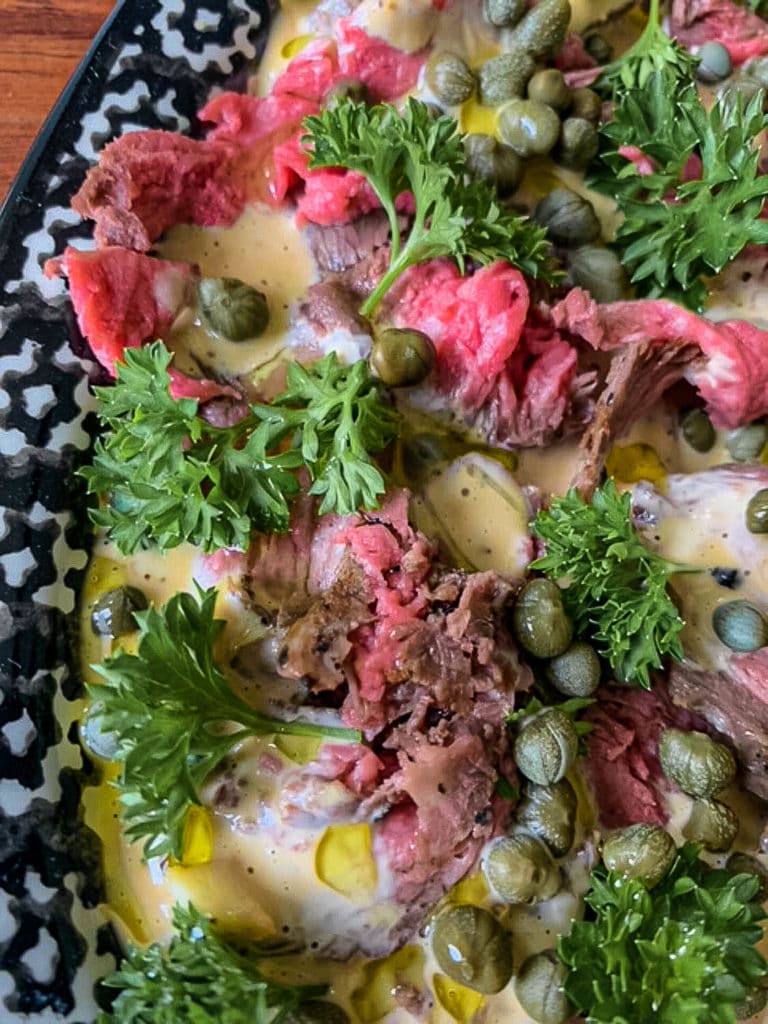 overhead close up picture of beef and parsley and capers on black platter