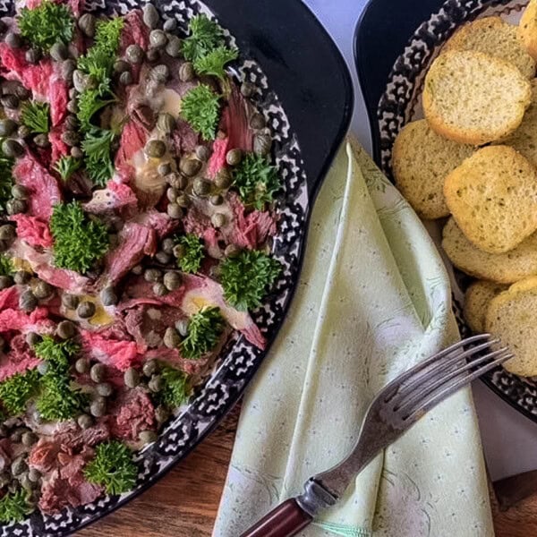 overhead picture of beef and parsley and capers on black platter