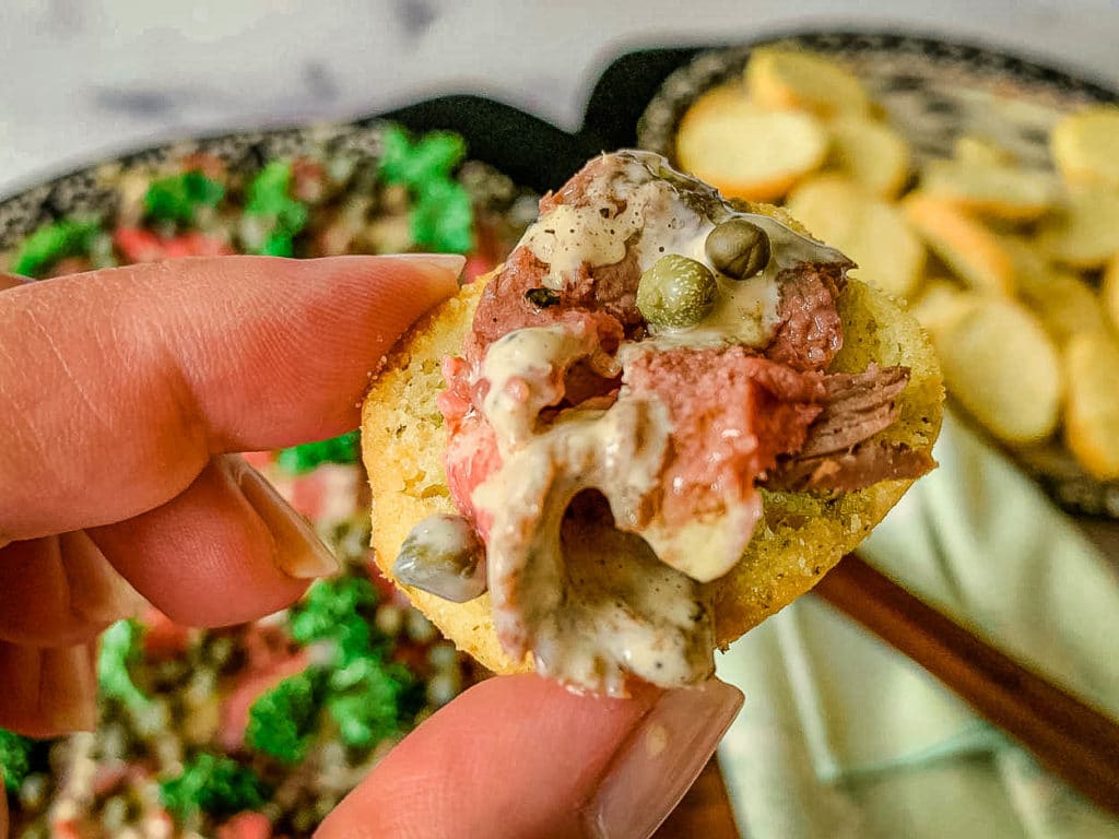 hand holding a cracker with carpaccio beef on it, with capers