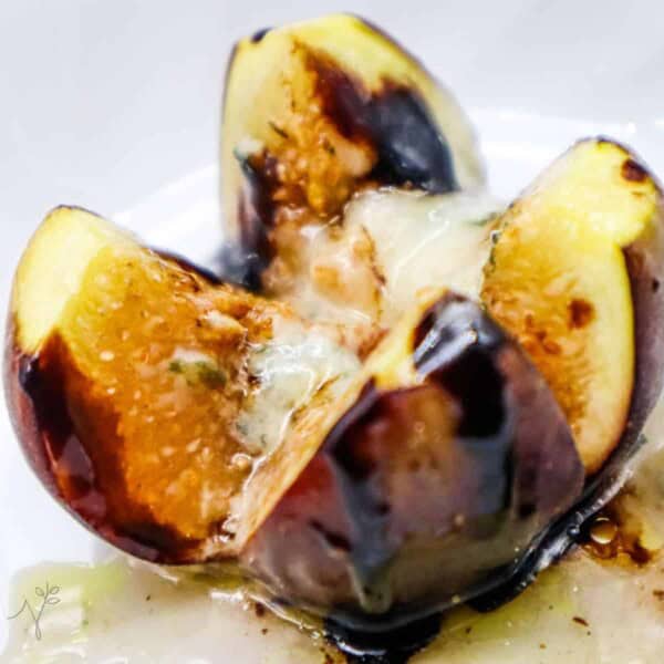 A baked fig with blue cheese and honey in a bowl with juices drizzled over the top.