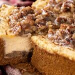 The image features a cheesecake with a thick graham cracker crust, topped with chopped pecans and a glossy caramel sauce. The dessert is partially sliced, showing its creamy interior.