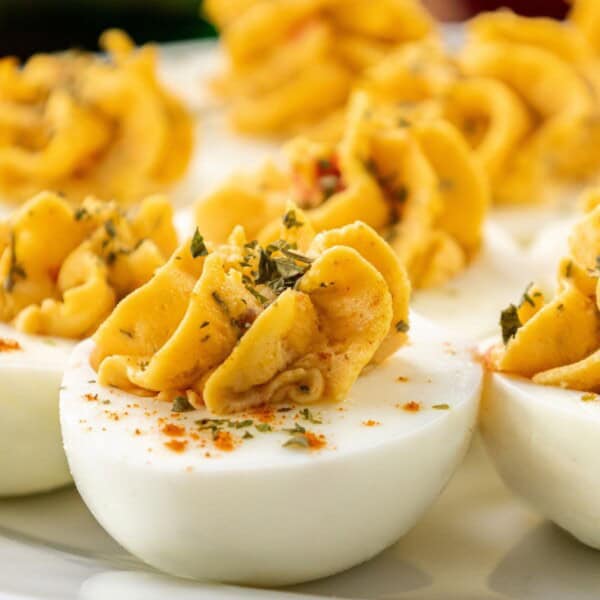 Pimento cheese deviled eggs with paprika and chopped herbs on top, set on a white plate.