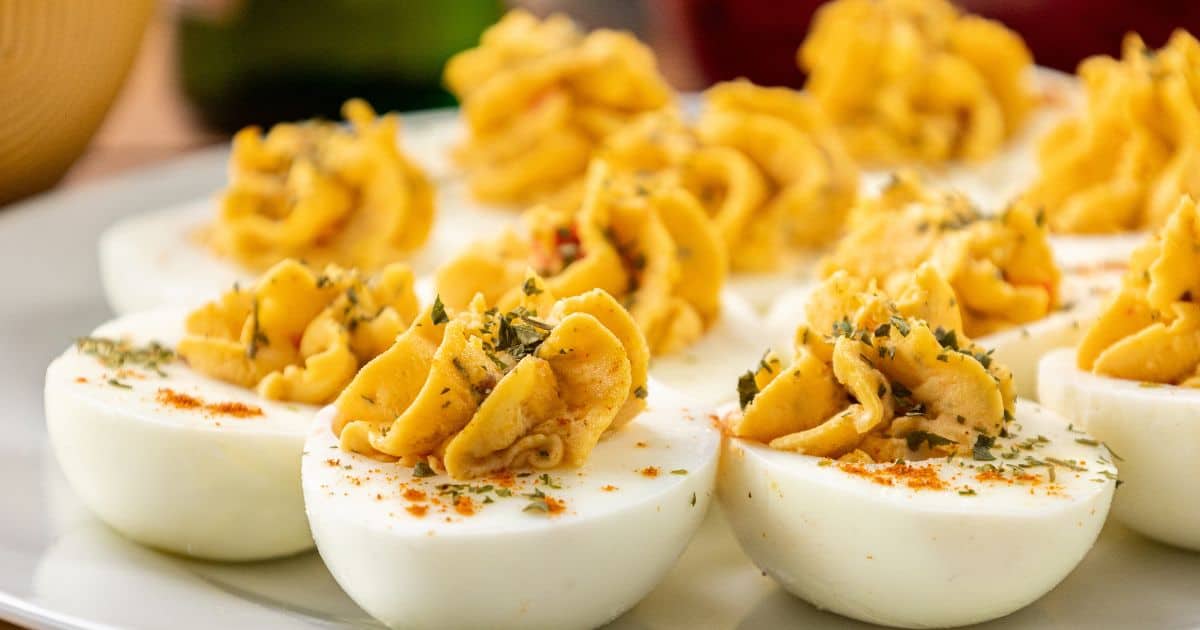 Deviled eggs with pimento cheese filling, sprinkled with paprika and herbs, are grouped on a white plate.