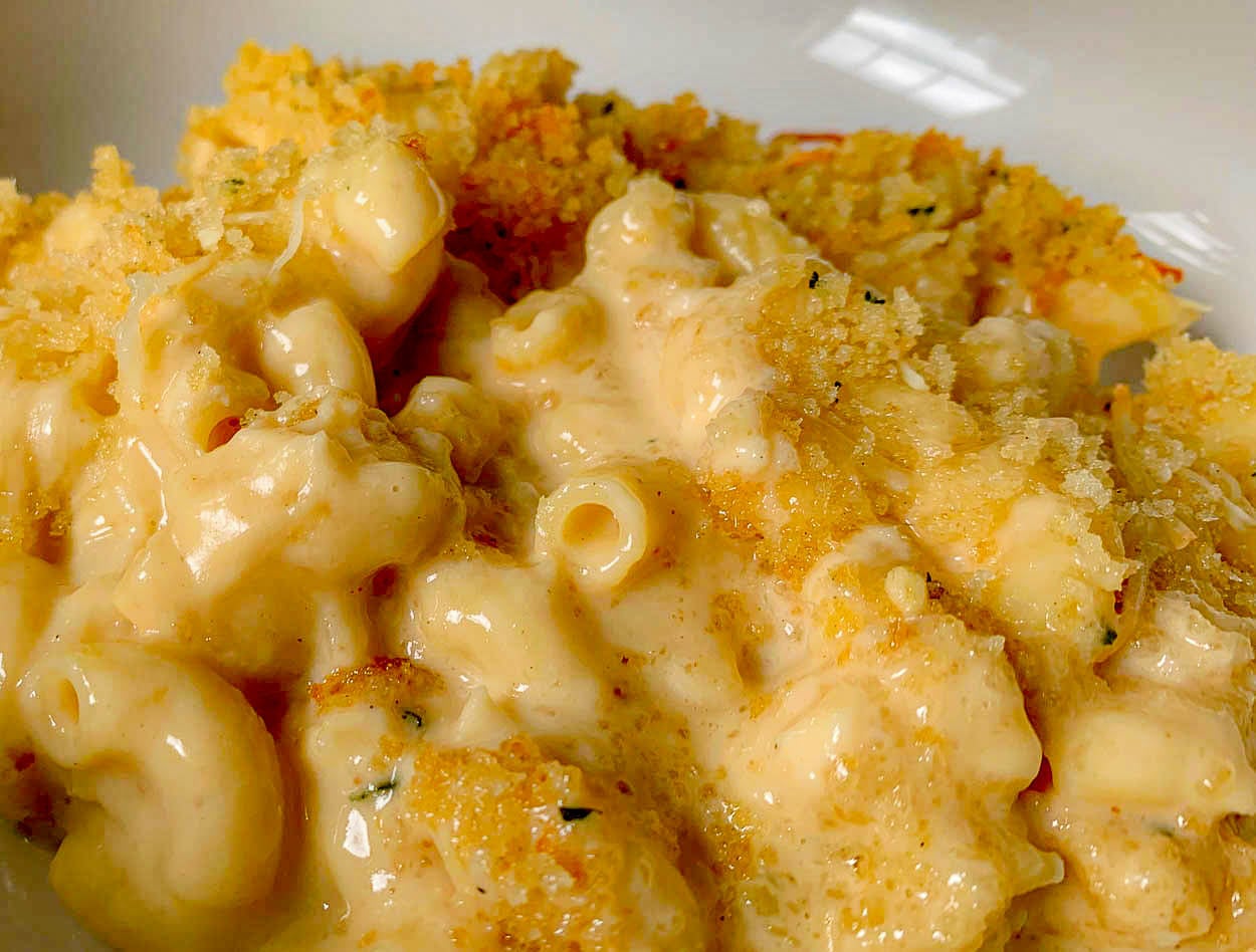 Close-up of a creamy macaroni and cheese dish topped with golden, crispy breadcrumbs. The cheese sauce is thick and velvety, coating the pasta perfectly. The breadcrumbs add texture, with a hint of herbs visible.