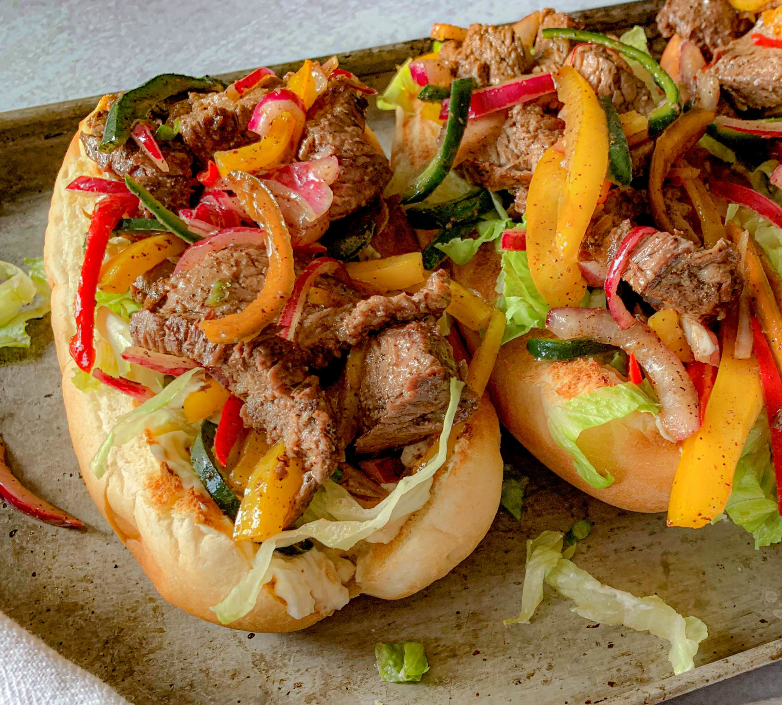 three steak hoagies on a broiler pan