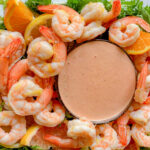 A platter of poached shrimp in citrus broth, with a bowl of zesty Louis sauce in the middle.