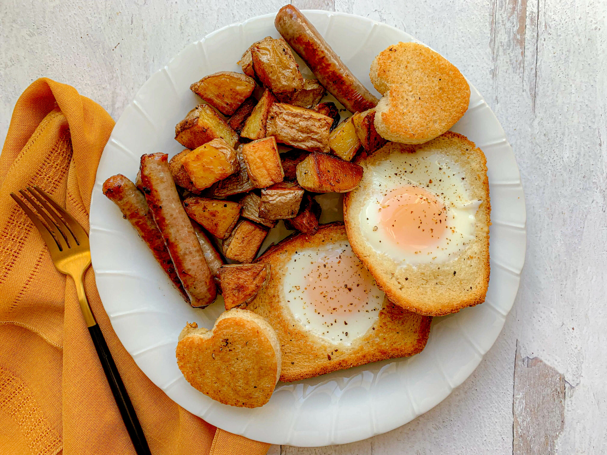 a white plate, with baked home fries, sausages and sunny eggs