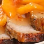 Close-up of sliced roasted pork topped with peach slices and drizzled with glossy bourbon BBQ sauce.