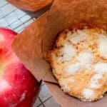 A warm Snickerdoodle muffin beside an apple on a cooling rack.