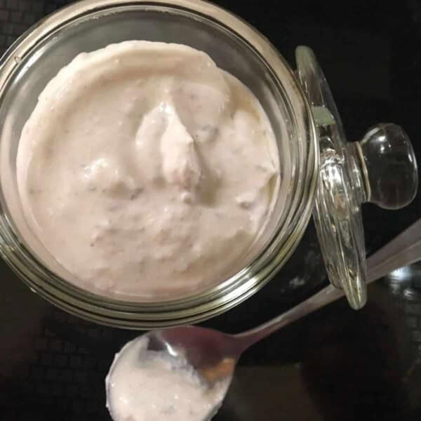 A tiny glass jar with a lid and a spoon, filled with a horseradish cream for beef and sandwiches.