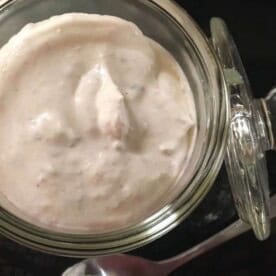 A small glass jar filled to the top with horseradish cream sauce and a spoon for serving.