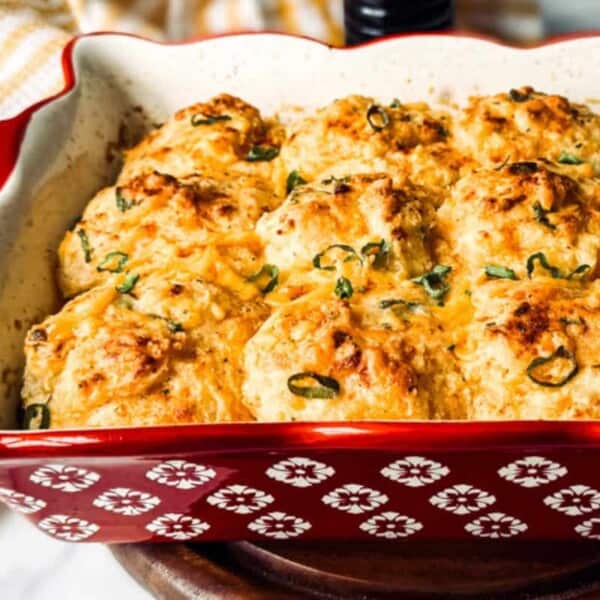 A red baking dish containing a golden-brown breakfast casserole topped with chopped green herbs.