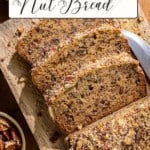Slices of banana nut bread are arranged on a wooden cutting board beside a dollop of sour cream. A knife rests nearby. Chopped nuts are scattered around, and a whole banana is visible in the background.