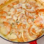 An enameled cast iron pan filled with sweet potatoes and cheese.