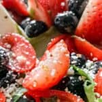 A platter heaped with fresh greens, ripe strawberries, and plump blueberries, with mozzarella and vinaigrette.