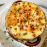 A soup crock filled with hot onion soup and topped with melted Gruyere cheese and fresh thyme.