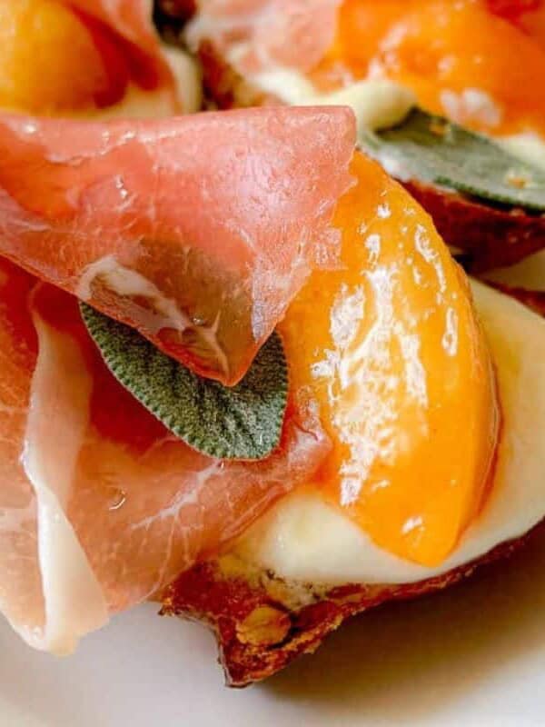 Honey Whipped Ricotta Crostini with Peaches and Prosciutto has honey drizzled over top and is on a serving dish.