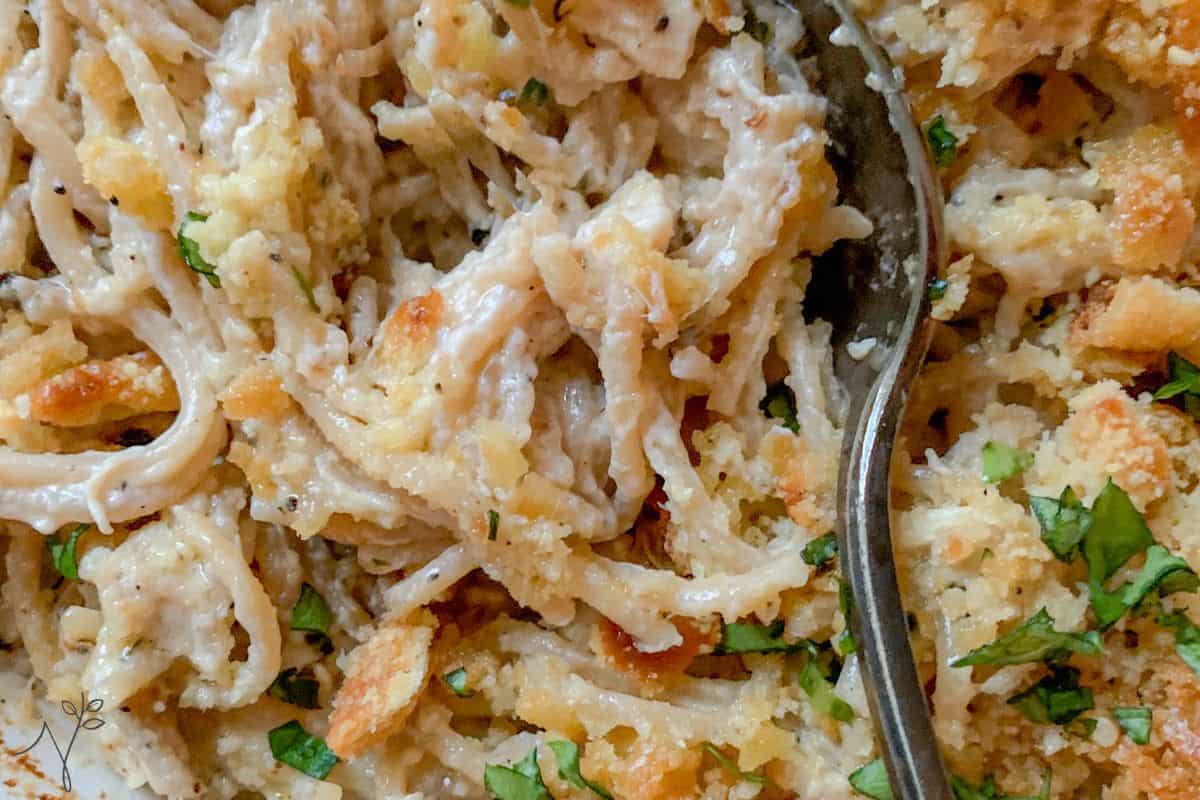 A creamy turkey tetrazzini garnished with chopped herbs and topped with breadcrumbs, with a partially visible metal fork in the dish.