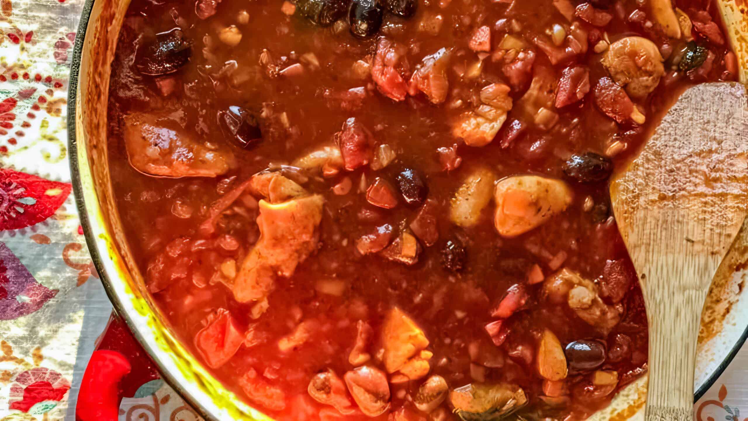 A Dutch Oven filled with hot Chicken Cacciatore with briny olives.