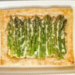 A puff pastry and cheese tart with asparagus on a serving platter.