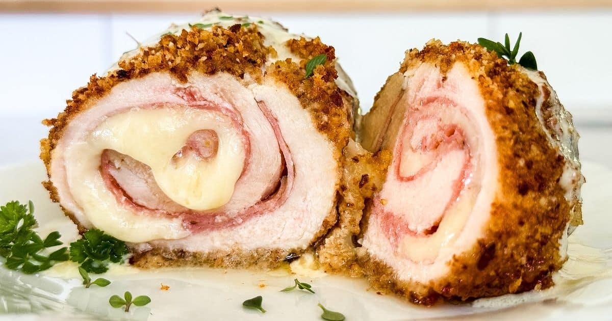 A close-up of sliced chicken cordon bleu. The dish features breaded and baked chicken breasts, stuffed with ham and melted cheese. The outer layer is golden brown and crispy, while the inside is juicy and filled with creamy cheese and ham layers.