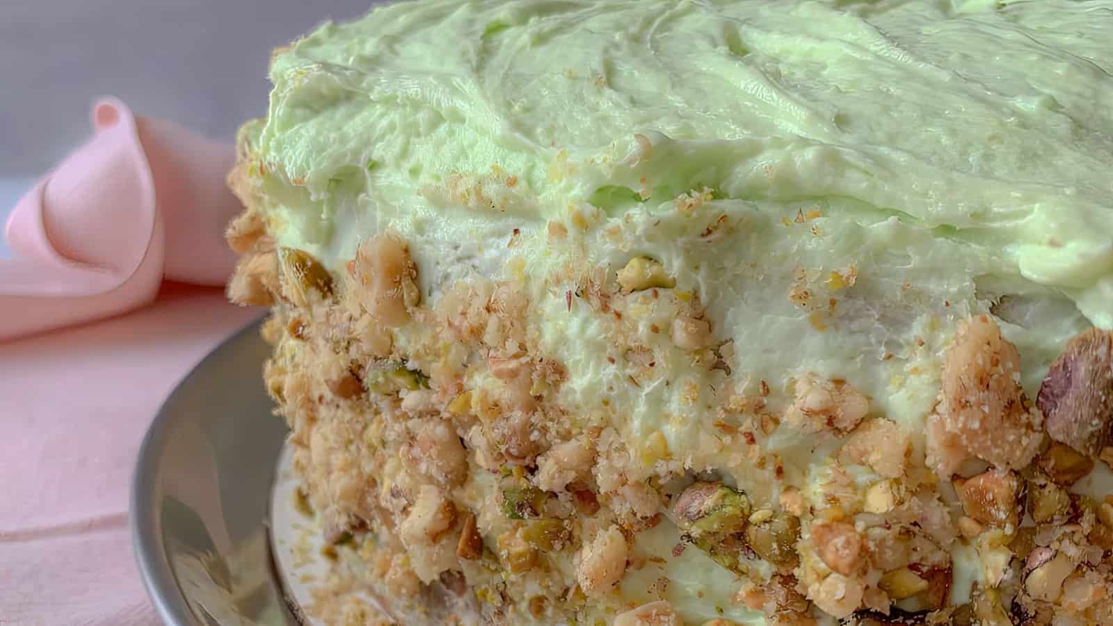 A layer cake with green frosting and chopped pistacho nuts.