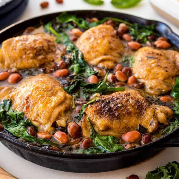 A cast iron skillet with a mustard chicken and beans.